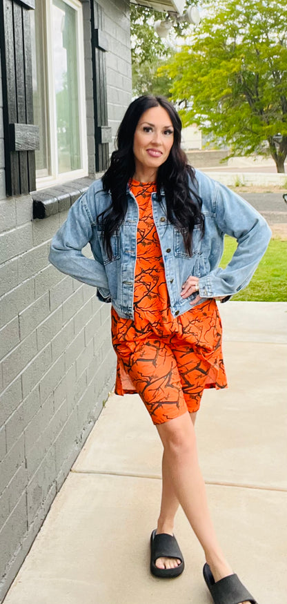 Woman wearing an orange outfit with a denim jacket standing on a sidewalk.