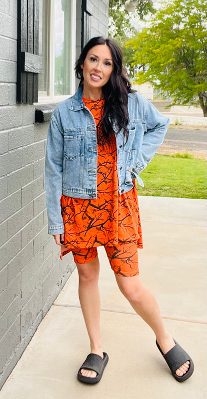 Woman wearing an orange dress with a denim jacket standing on a sidewalk.