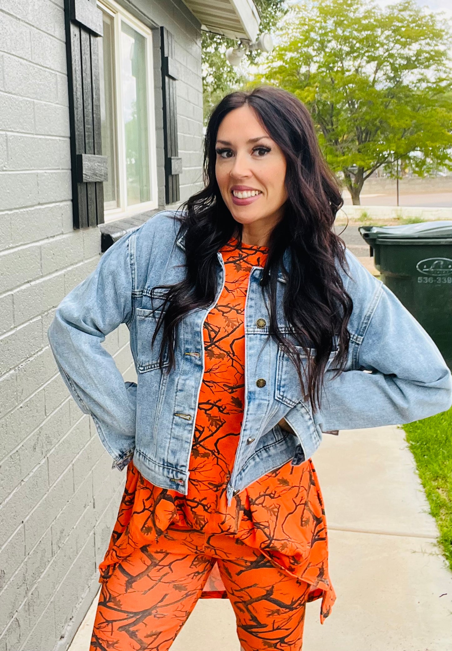 Woman wearing an orange and black patterned outfit with a denim jacket outdoors.