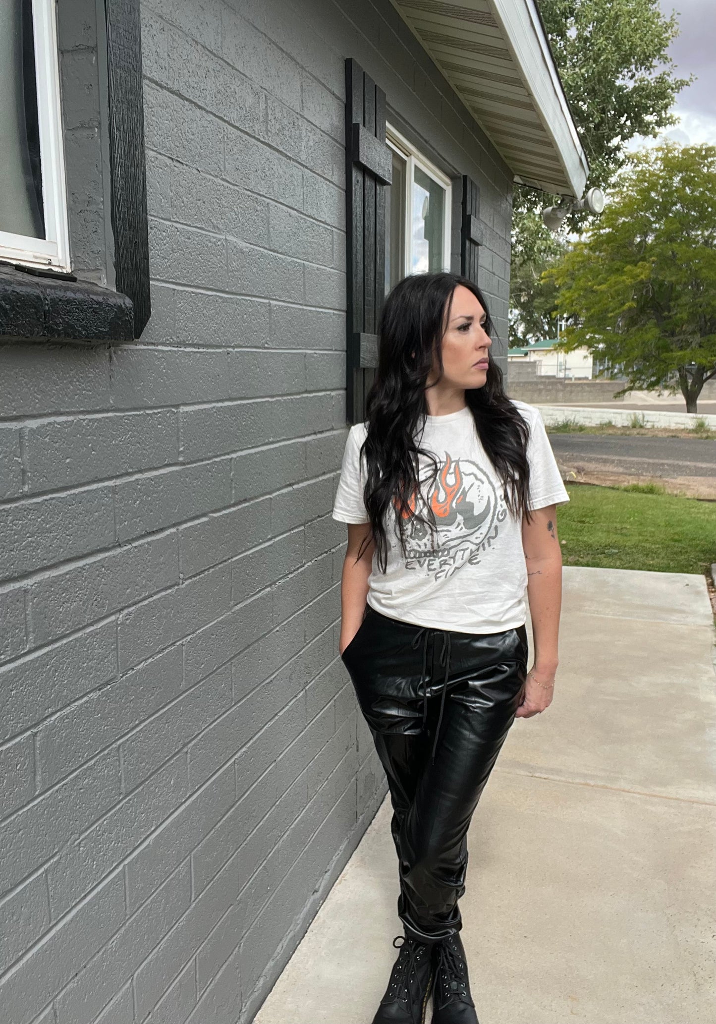Person wearing a graphic t-shirt and black leather pants standing against a gray building.