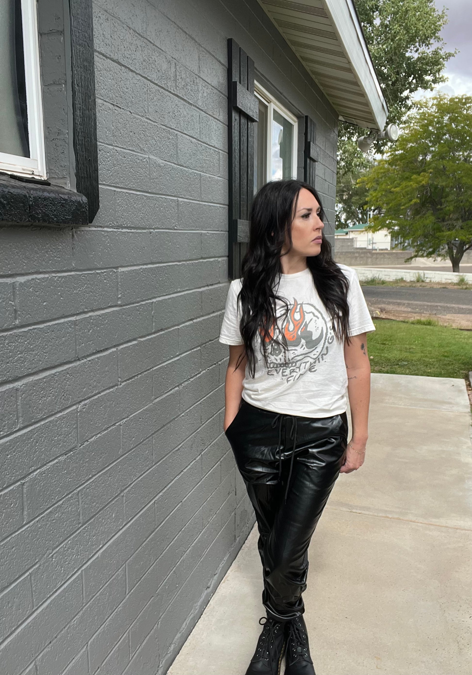 Person wearing a graphic t-shirt and black leather pants standing against a gray building.