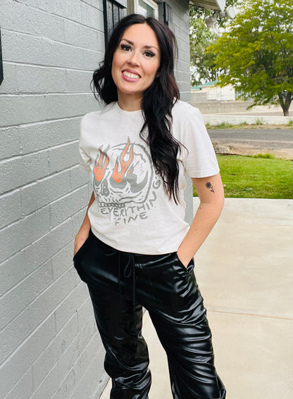 Woman wearing a graphic t-shirt and black pants standing against a gray wall.