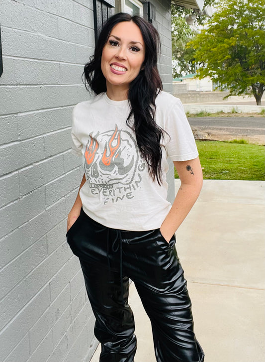 Woman wearing a graphic t-shirt and black pants standing against a gray wall.