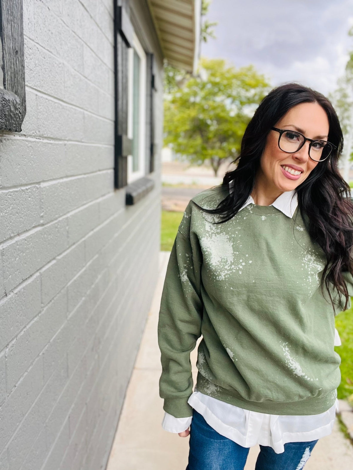 Woman wearing a green sweatshirt with white splatter design outdoors.