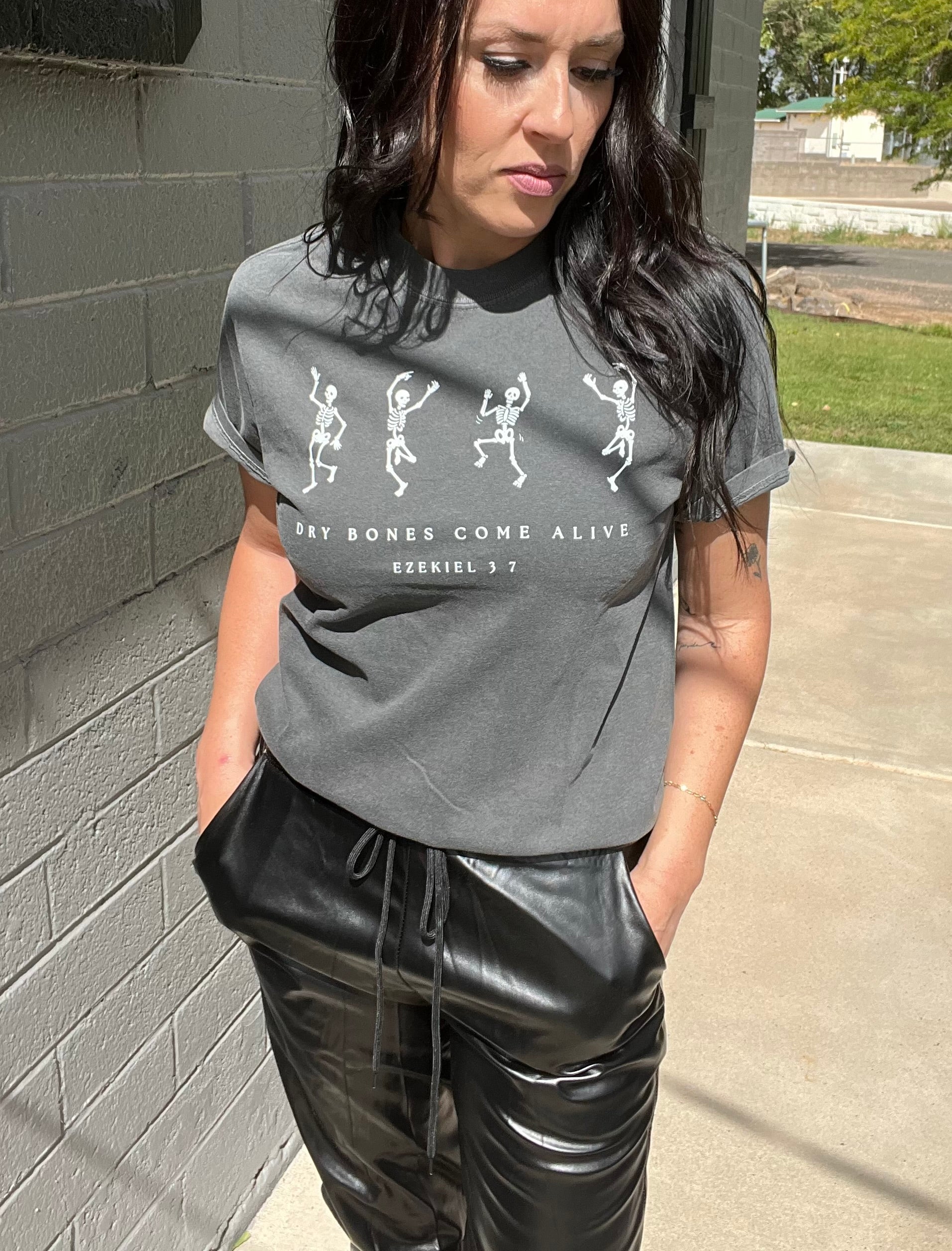 Person wearing a gray t-shirt with graphic design and text, standing against a brick wall.