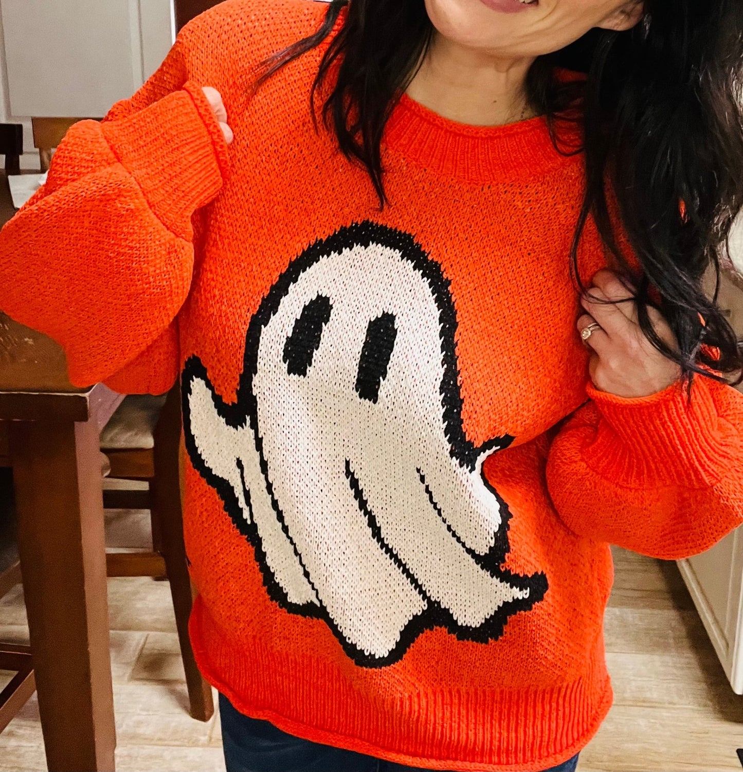 Person wearing an orange sweater with a ghost design indoors.