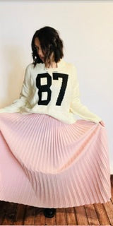 Person wearing a white sweater with the number 87 and a pink pleated skirt.