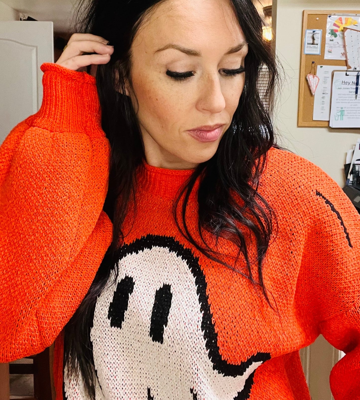 Woman wearing an orange sweater with a cartoon character design, indoors.