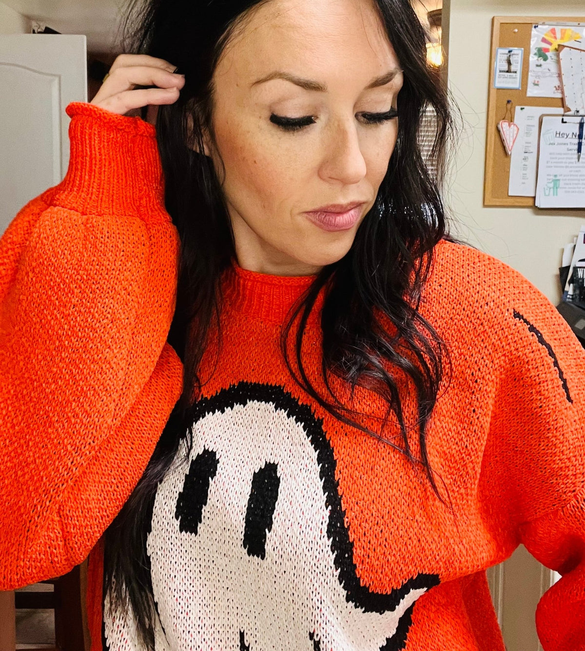Woman wearing an orange sweater with a cartoon character design, indoors.