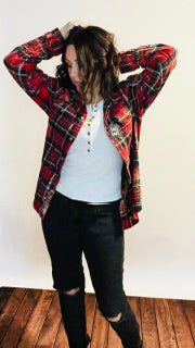 Person wearing a red plaid shirt over a white top and black pants on a wooden floor.
