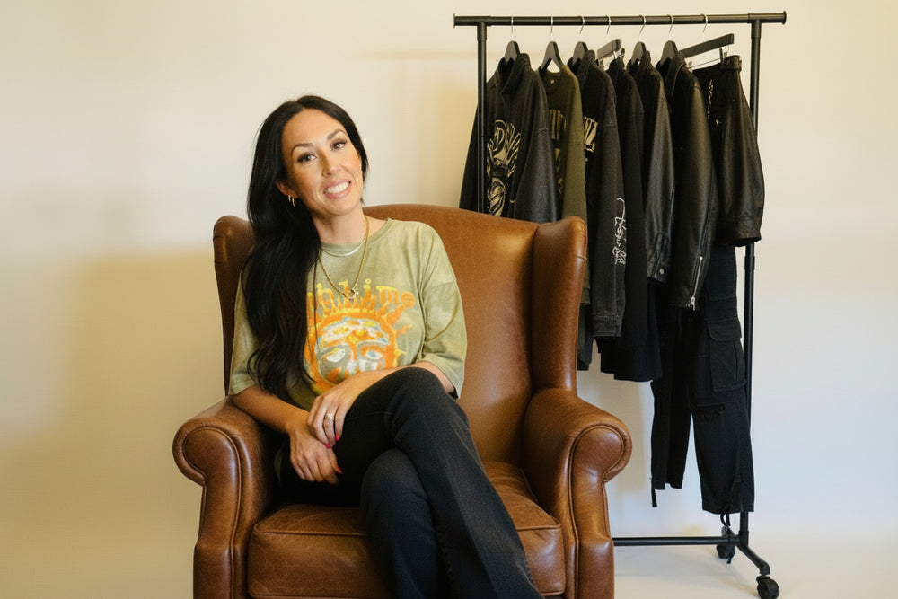 Woman sitting on a wooden chair wearing a green t-shirt with a graphic design and dark jeans.