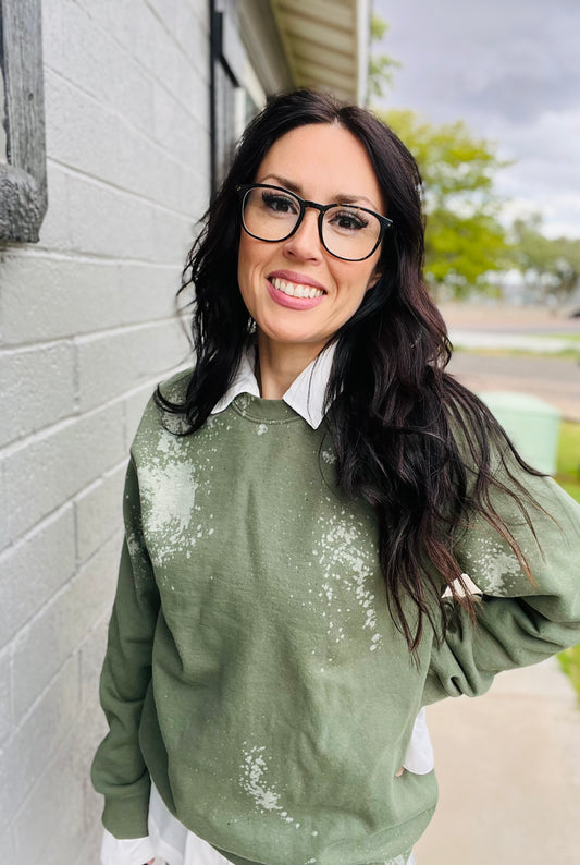 Woman wearing a green bleached sweater standing against a gray wall.