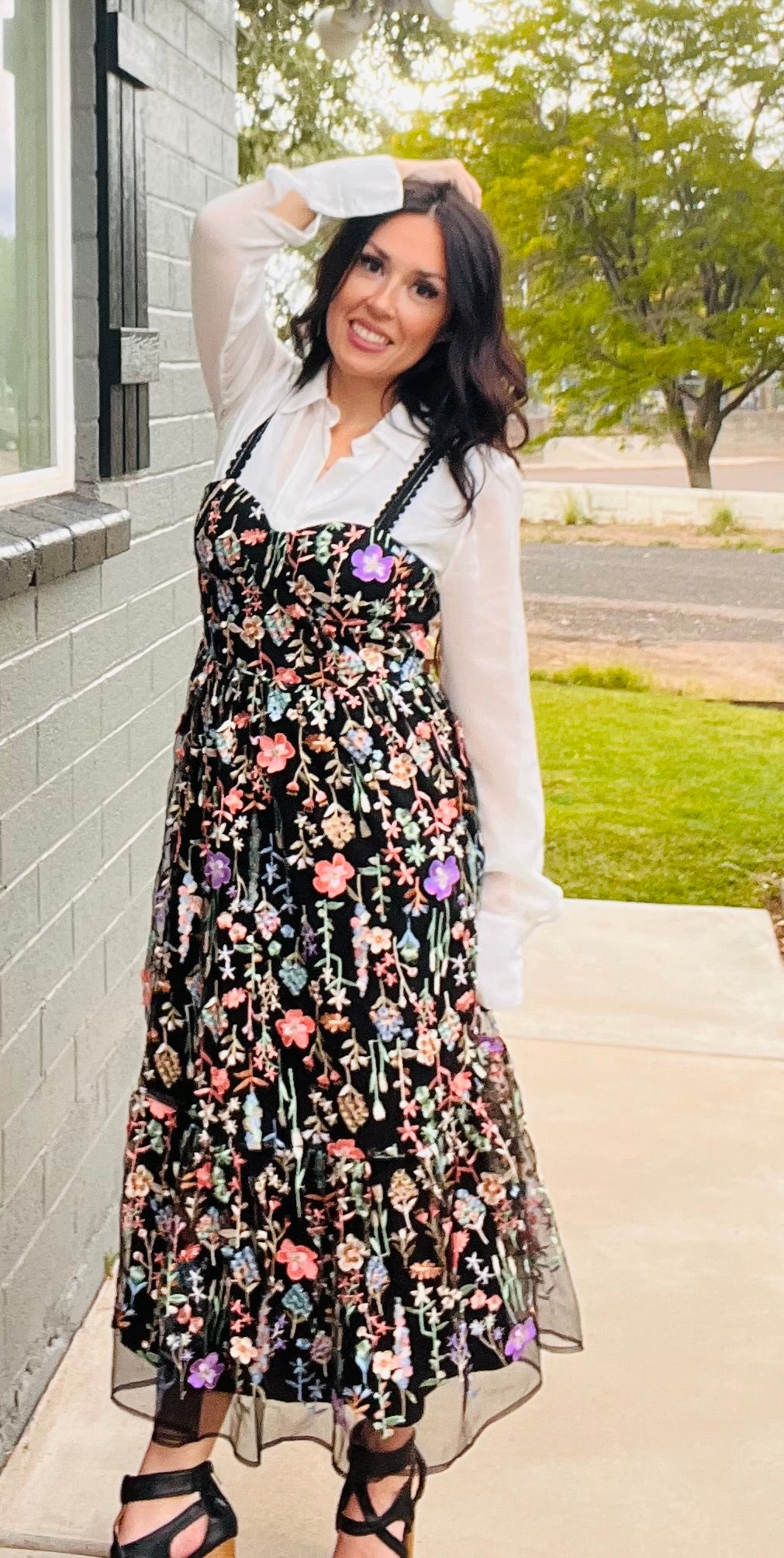 Woman wearing a floral dress with a white shirt and black shoes outdoors.