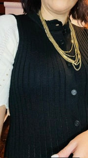 Person wearing a black dress with white sleeves and gold necklace.