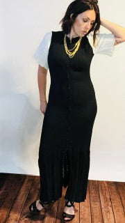 Woman wearing a black dress with white sleeves against a white wall.