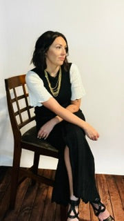 Person wearing a black dress with white sleeves and gold necklace sitting in a chair